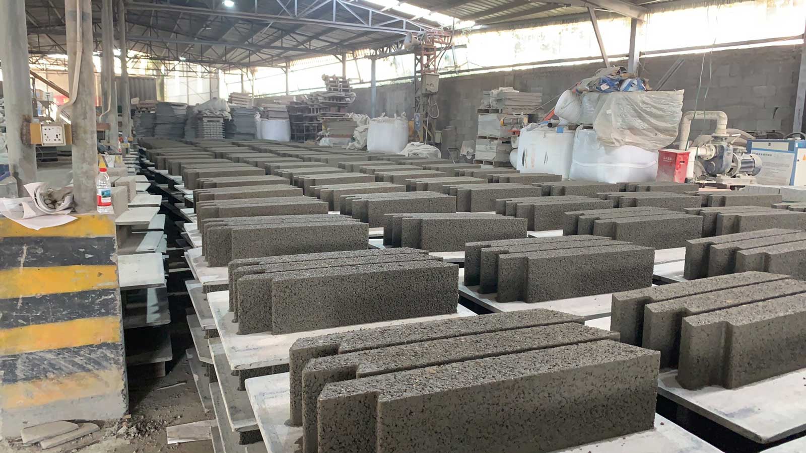 标准化车间内正在成批静停养护的灰色预制硅砂模块，展现海绵城市建材的精细生产工艺