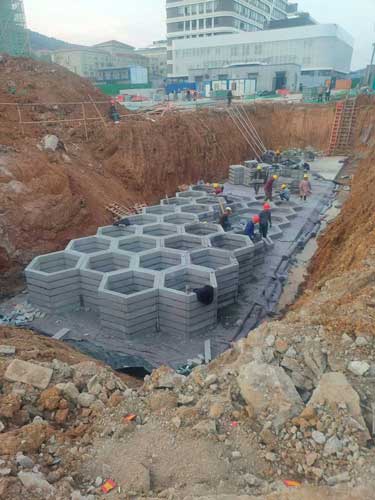 建筑工地深基坑内多名工人正在合力拼装组装的蜂巢状地下硅砂雨水收集池