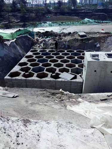 大型地下硅砂雨水收集池，展现大面积壮观且规整的六边形蜂巢网格构造与相邻的混凝土泵房