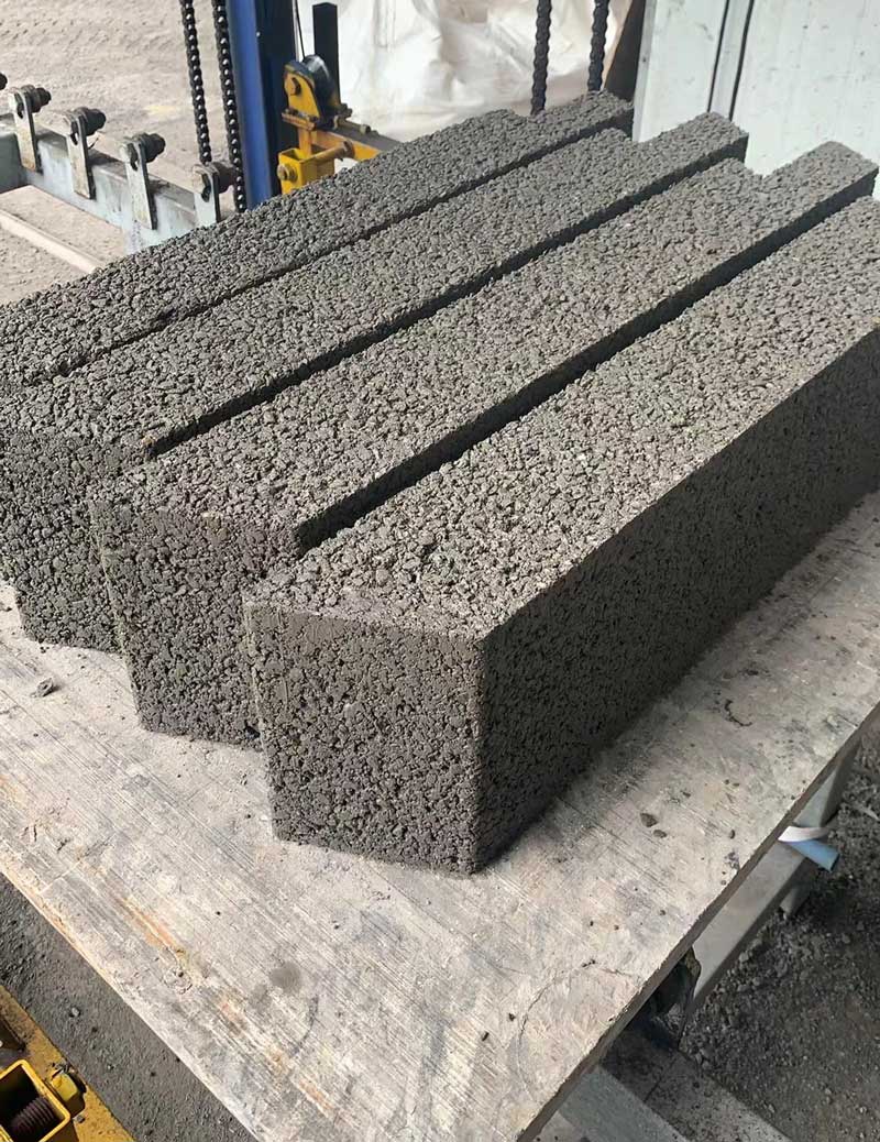 近景特写呈并排摆放的深灰色多孔硅砂砌块，表面具有强烈的透水骨料颗粒质感与拼装切角
