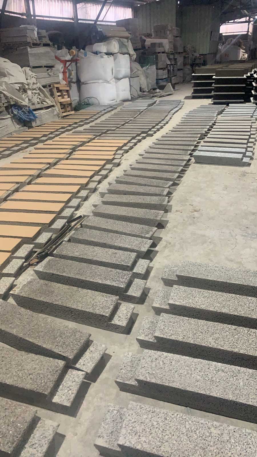 宽敞的工业厂房内，水泥地面上纵向铺满了数行正在养护的复合硅砂透水砖模块