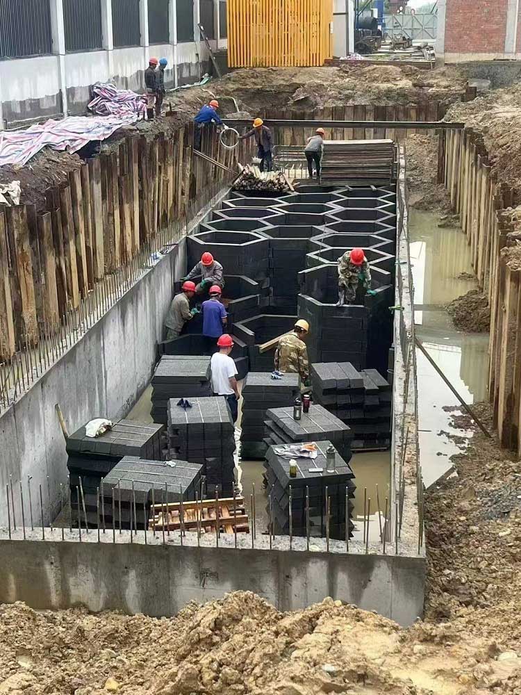 混凝土基坑内，工人们正在搬运并拼装蜂巢状地下硅砂雨水蓄水池