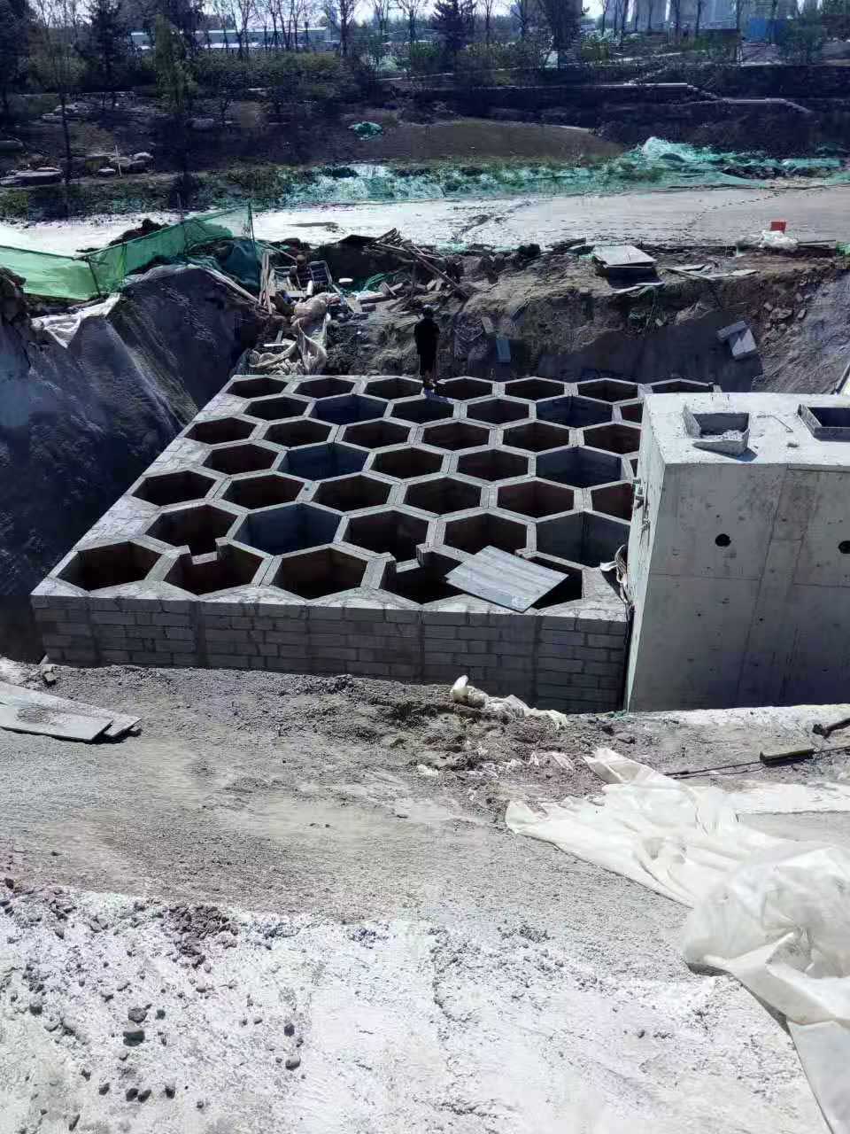 大型地下硅砂雨水收集池,展现大面积壮观且规整的六边形蜂巢网格构造与相邻的混凝土泵房 大型地下硅砂雨水收集池,展现大面积壮观且规整的六边形蜂巢网格构造与相邻的混凝土泵房